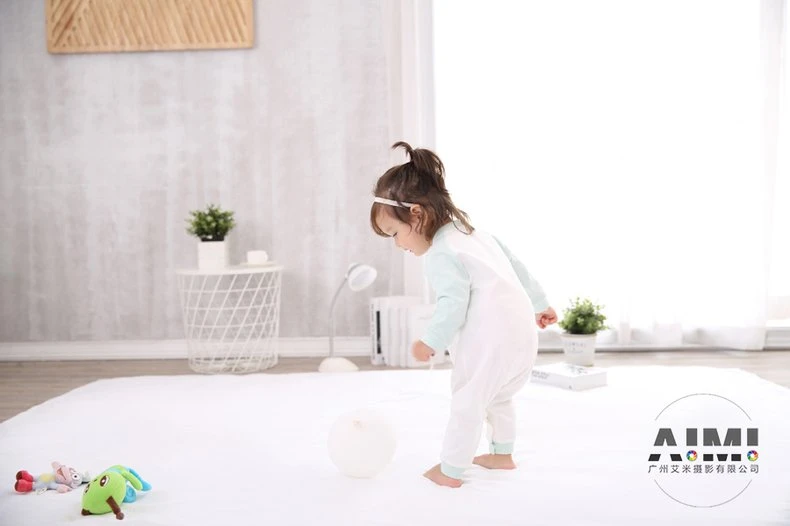 Toddler in a raglan romper standing before a white play ball on a nursery set
