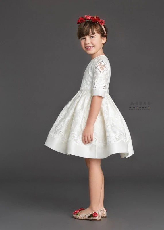 Profile of a child model in an ivory damask cutwork dress with red flower crown and floral flats