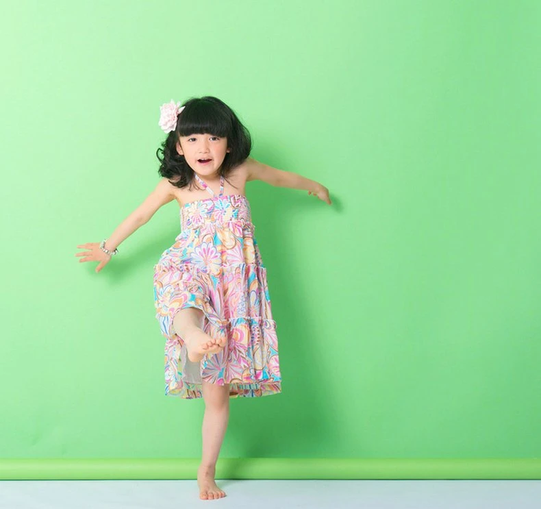 Child model in a retro pastel floral halter sundress mid-kick on a green backdrop