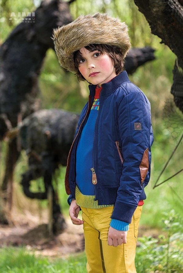 Boy model in a navy quilted bomber, fur ushanka and mustard chinos in a woodland setting