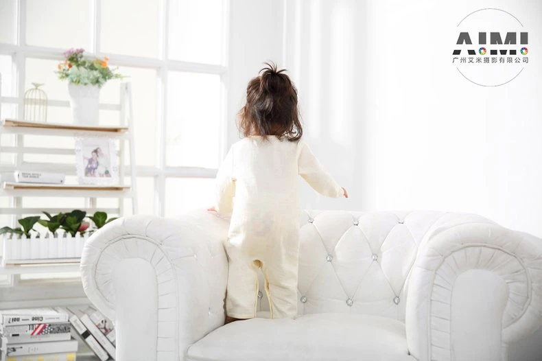Full back view of a toddler in a cream muslin romper standing on the sofa cushion
