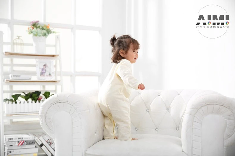 Toddler in a cream romper standing three-quarter back on the white sofa