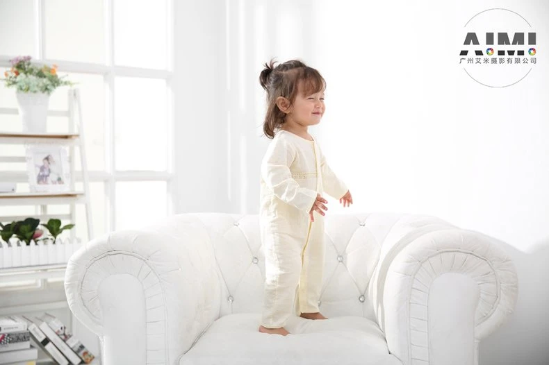 Toddler in a cream romper standing on the chair laughing in profile