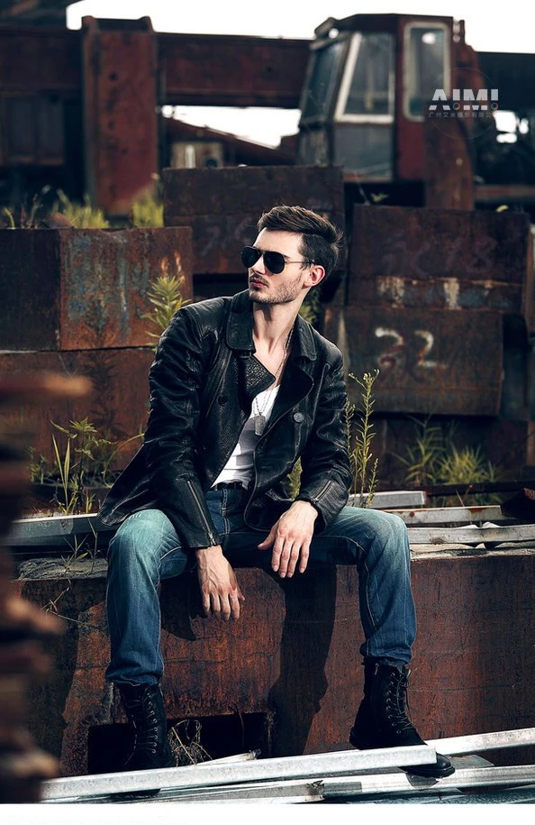 Model in a distressed black biker jacket seated on rusted steel slabs at golden hour