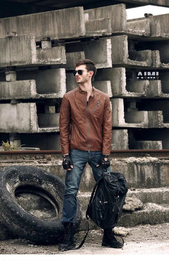 Model in a cognac brown moto jacket with one boot on a discarded tire, concrete block stacks behind