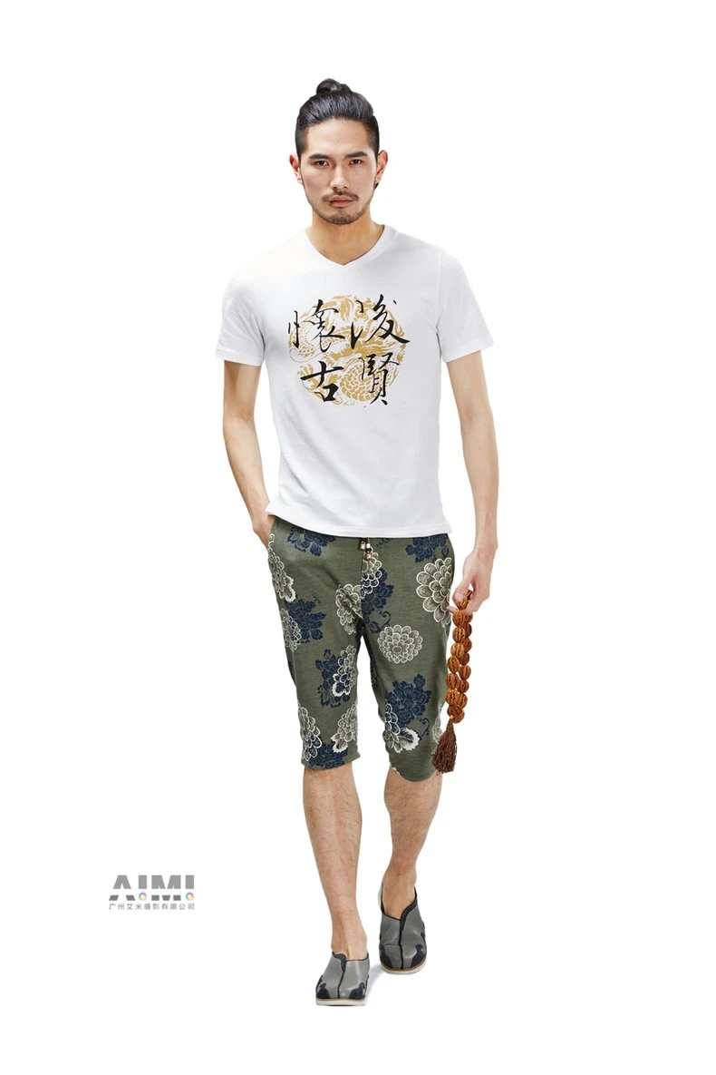 Model in a calligraphy-print white tee and olive floral capri shorts holding a wooden mala strand