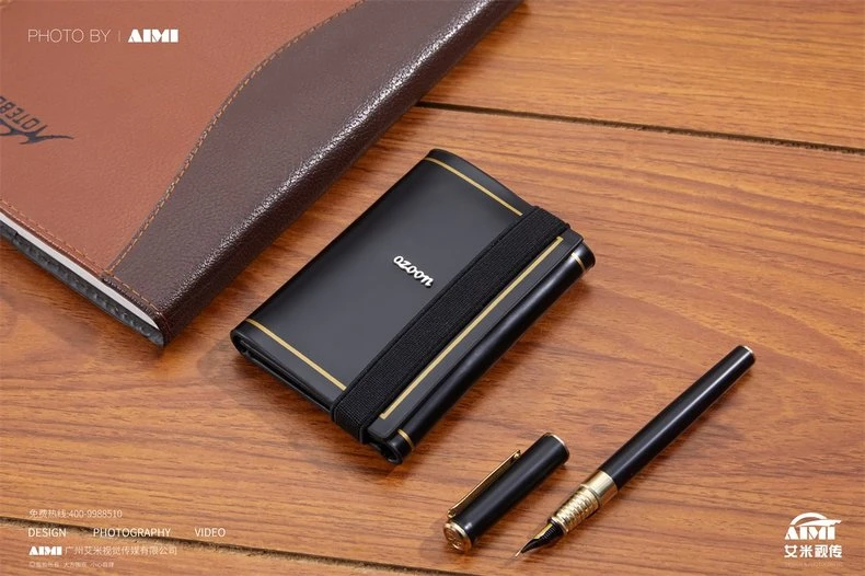 Black glossy card case with elastic band and gold pinstripe - three-quarter desk product photography