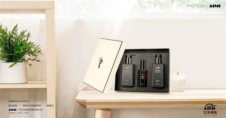 Three-piece personal care gift set in an ivory presentation box with two matte black pump bottles and an amber glass bottle, warm window-light photography