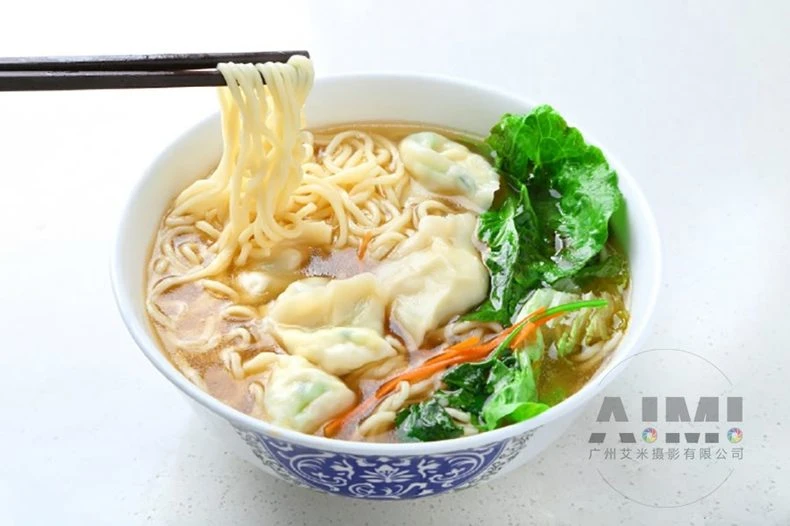 Wonton noodle soup in clear broth with greens in a white bowl