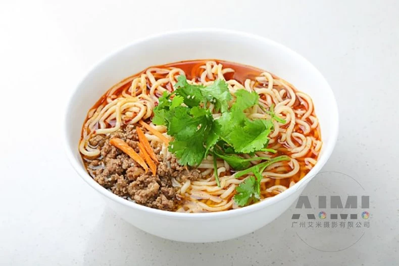 Spicy red oil noodles with scallion and sesame in a white bowl