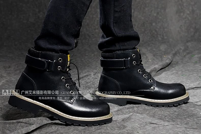 Black leather lace-up work boots with beige welt stitching worn on-foot against a crumpled gray backdrop