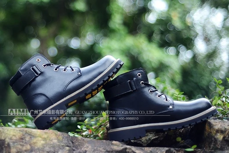 Black leather hiking boots resting on rough rocks with soft green bokeh, outdoor side-profile frame