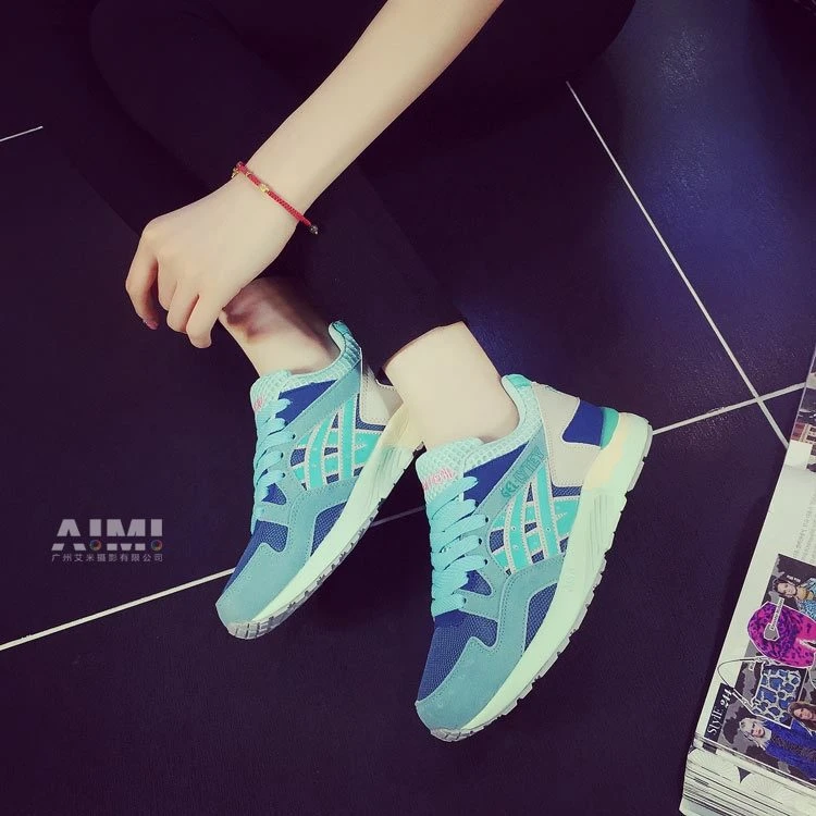 Navy and mint color-blocked retro running sneakers worn on-foot with black leggings on a dark tiled studio floor