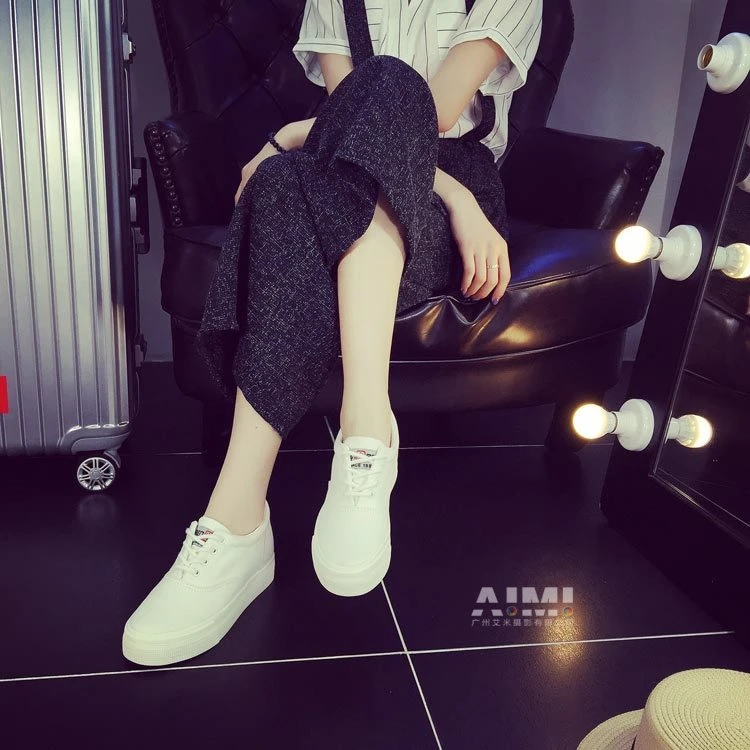 White platform canvas sneakers on a seated model, dressing-room set with vanity mirror bulbs and rolling suitcase
