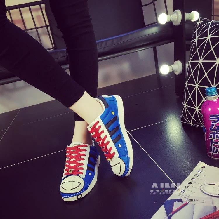 Blue and white cartoon-character canvas sneakers with red laces and a small bell charm, low on-foot frame