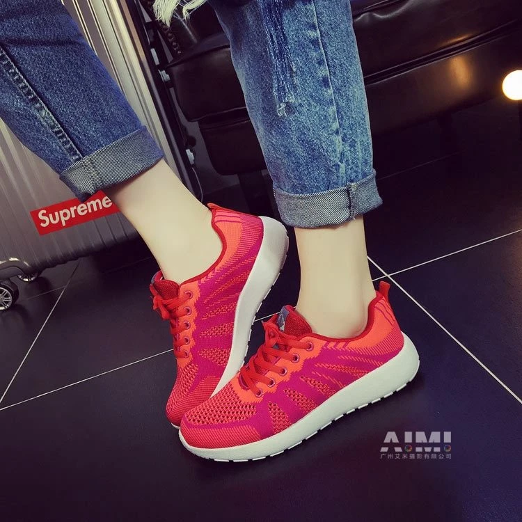 Red-to-fuchsia gradient knit sneakers with white soles, lifted-foot on-foot pose