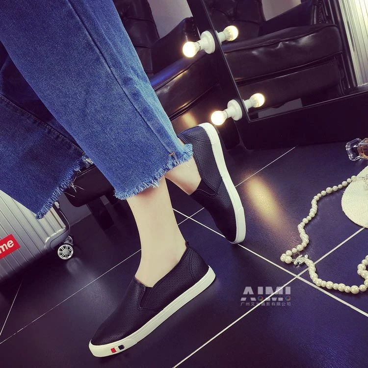 Black slip-on leather sneakers with off-white soles, styled with pearl and perfume props