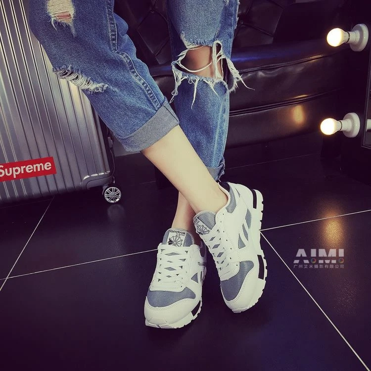 White and gray platform sneakers with distressed cuffed jeans in a crossed-leg pose