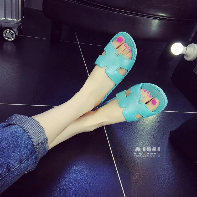 Turquoise H-cutout flat slide sandals on crossed ankles, high-angle first-person view