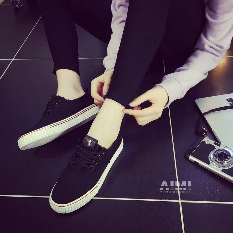 Black canvas sneakers with red side stripe and metallic star heel tag, styled with a retro camera prop