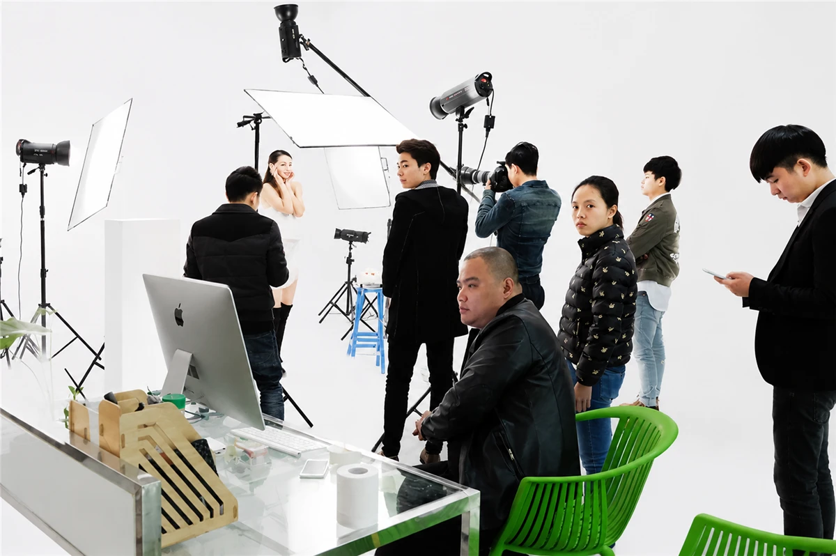 AIMI crew reviewing frames on the tethered station while the model holds a pose on the white cyclorama
